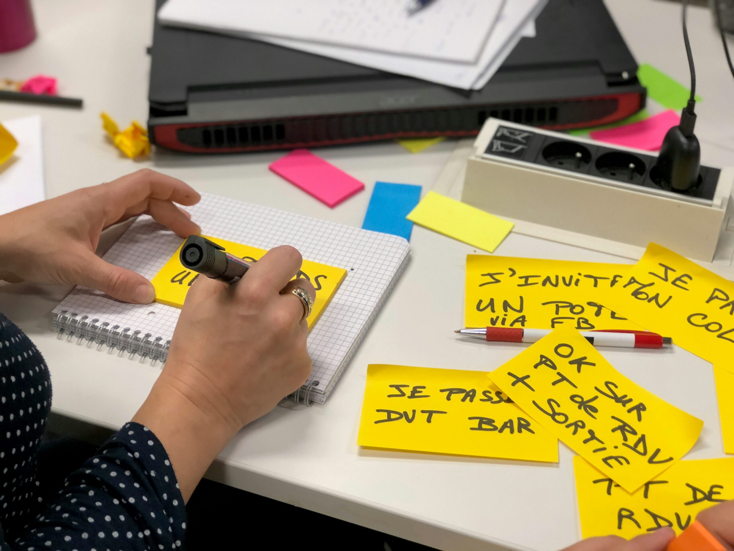 Mani che scrivono appunti su carta e post-it accanto a un laptop con uno strumento AI aperto, a rappresentare l'organizzazione del lavoro che accompagna l'uso dell'intelligenza artificiale